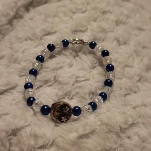 Armband med blå och klara pärlor - Charmigt armband med växelvis blå och klara pärlor. Armbandet har en silverfärgad berlock med stjärnmotiv. Perfekt för att ge en färgklick till din outfit.