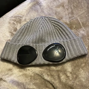 Grå C.P Company mössa - Vanlig mössa från C.P Company, den är otroligt skön att ha på sig. Mössan är ljusgrå och i bra skick, den ska vara unisex och passa alla olika huvuden. Kollade bara snabbt bad den såldes för och kom fram till mellan 550-750 kr ungefär, så jag har ingen aning om vad jag ska sälja den för därför har jag bestämt att sålja den för 450 kr. Är du intresserad tveka inte på att skriva och komma med ett bud! 