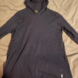 Mörkblå hoodie från Ralph Lauren - Säljer en stilren mörkblå hoodie från Ralph Lauren med den klassiska loggan broderad i vitt. Tröjan har långa ärmar och en praktisk huva med dragsko. Perfekt för en avslappnad look. Hör av dig vid intresse