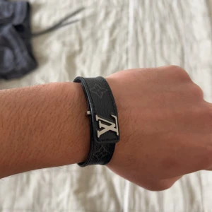 Svart läder armband från Louis Vuitton. Äkta! - Snyggt svart armband i läder med ett stilrent metallspänne. Perfekt accessoar för att ge en elegant touch till din outfit. Armbandet har justerbara hål för att passa olika handledsstorlekar.