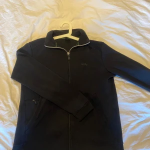 Svart zip tröja från Boss - Snygg svart ziptröja från Boss med dragkedja och långärmad design. Perfekt för en stilren look. Tröjan är i väldigt bra skick, ser inga tecken på användning. Storlek S men passar också Medium