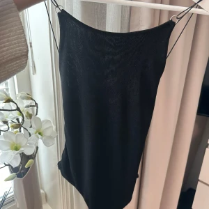 Svart axelbandslös body - Snygg svart body med smala axelband och öppen rygg. Perfekt för en kväll ute eller en speciell tillställning. Enkel och elegant design som passar till många olika stilar. Aldrig använd från nelly