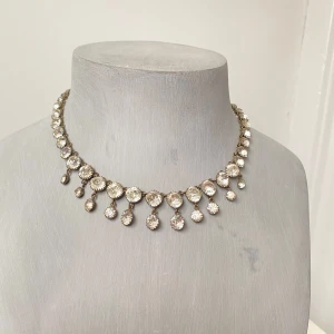 Glittrigt vintage halsband med stenar - Elegant halsband med glittrande stenar i en droppformad design. Halsbandet har en klassisk kedja med små, gnistrande stenar som hänger i olika längder, vilket ger en lyxig känsla. Perfekt för att lägga till lite glamour till din outfit. Vintage. Elegant låsanordning