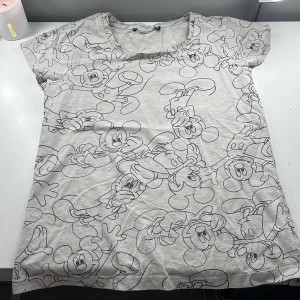 Grå t-shirt med Musse Pigg-mönster - Säljer en grå t-shirt från Disney med ett coolt Musse Pigg-mönster över hela tyget. T-shirten är kortärmad och har en rund halsringning. Är i storlek xs tror jag men passar även barn. Den är ifrån New yorker