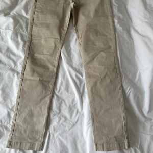 Snygga klassiska Beige chinos - Snygga beige chinos i bomull med en liten del elastan för extra komfort. De har en klassisk design med knappar och bälteshällor, perfekt för en stilren look. De har en medelhög midja och räcker ner till hälen på mig som är 1,63 lång.
