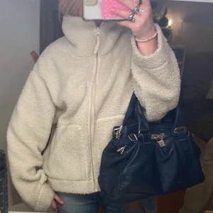 Vit / Beige teddyjacka Hm - Mysig beige teddyjacka med dragkedja framtill. Jackan har en hög krage och långa ärmar, perfekt för kyliga dagar. Den har en avslappnad passform som ger en skön och trendig look.