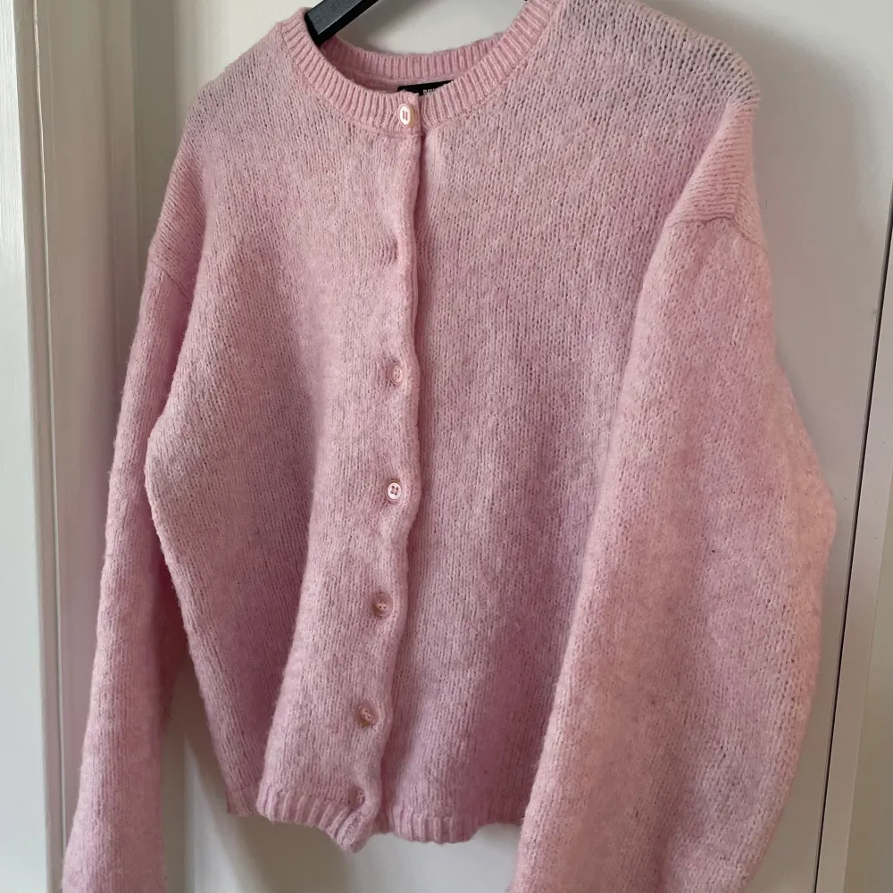 Mysig rosa stickad kofta från BikBok med knappar framtill. Perfekt för kyliga dagar och ger en söt touch till din outfit. Koftan har långa ärmar och en rund halsringning. Sitter som en S/M. Liten i storleken.. Neuletakit & Villapaidat.