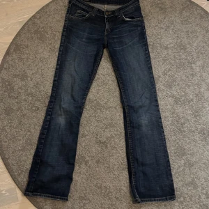 Mörkblå bootcut jeans från Lee - Snygga lågmidjade mörkblå jeans från Lee med klassisk femficksdesign. De har en bootcut passform och är perfekta för en avslappnad stil. Jeansen har en knapp och dragkedja framtill. Hör av er om ni har några frågor!💖 Priset kan även diskuteras