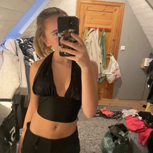 Svart halterneck topp - Snygg svart halterneck topp med djup urringning och croppad design. Perfekt för en kväll ute eller en fest. Toppen har en stilren look och är lätt att matcha med olika outfits.