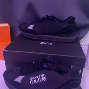 Svarta sneakers från Versace Jeans Couture - Snygga svarta sneakers från Versace Jeans Couture med vit logga på sidan. Skorna har en stilren design med snörning och en bekväm sula. Perfekta för en trendig look.