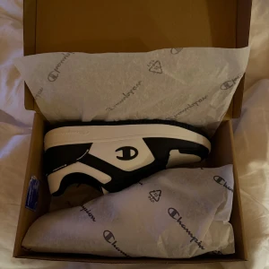 Svartvita sneakers från Champion - Snygga svartvita sneakers från Champion med märkets logotyp på sidan. Skorna har en klassisk design med snörning och en bekväm sula. Perfekta för en stilren look.