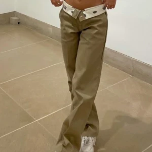 Beige byxor från Dickies - Snygga beige byxor från Dickies med en klassisk design. Byxorna har en rak passform och är tillverkade i slitstarkt material. Perfekta för en avslappnad stil med en vit kontrastdetalj vid midjan.