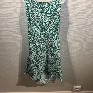 Grön blommig klänning från Shein - Säljer en söt grön klänning med vita blommor från Shein. Klänningen har en öppen rygg med snörning. Perfekt för sommarens alla tillfällen! 🌸