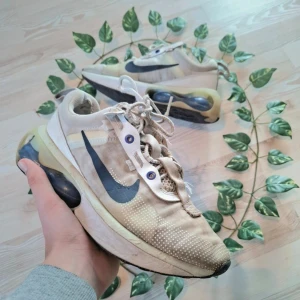 Beige Nike sneakers med blå detaljer - Säljer ett par beige Nike sneakers med blå swoosh och prickigt mönster. Skorna har synlig luftdämpning i sulan och snörning framtill. Perfekta för en sportig look.