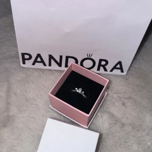 Silverring med stenar från Pandora - Elegant silverring från Pandora med glittrande stenar i en kronliknande design. Perfekt för att ge en touch av glamour till din stil. Ringen kommer i en fin rosa ask.
