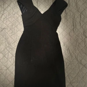 Svart klänning från Zara - Elegant svart klänning från Zara med en figurnära passform och djup v-ringning. Klänningen har en dragkedja i ryggen och är ärmlös, vilket ger en stilren look. Perfekt för en kväll ute eller en speciell tillställning.