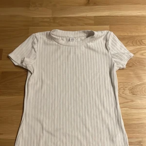 Vit t-shirt -  Säljer en vit ribbad t-shirt från Lindex i storlek 146/152 men passar även XS. Det är en tajt modell och t-shirten är i bra skick ⭐️