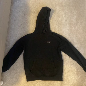Svart hoodie från Levi's passar mellan 11-14 år typ - Säljer en klassisk svart hoodie från Levi's i storlek XXS. Den har en justerbar huva och en praktisk magficka framtill. Perfekt för en avslappnad stil. Levi's-loggan är diskret placerad på bröstet.