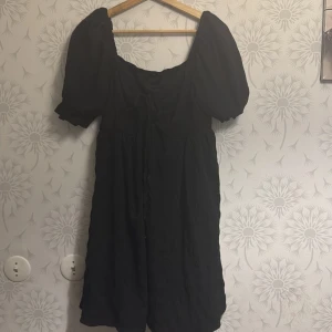 Svart klänning med puffärmar - Säljer en stilren svart klänning med puffiga kortärmar och en söt knytning framtill. Perfekt för en chic look. Klänningen har en luftig passform och är gjord i ett mjukt material.