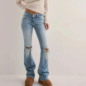 Populära jeans från nelly💗💗 - Snygga ljusblå bootcut jeans med slitningar på knäna. De har en låg midja och klassiska femficksdetaljer med knappar på bakfickorna. Perfekta för en avslappnad stil. Aldrig andvända
