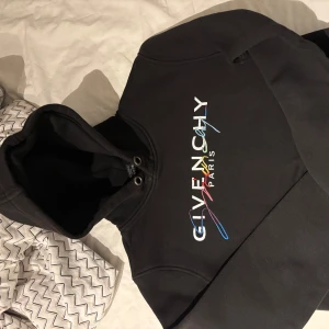 Svart hoodie  Givenchy - Snygg svart hoodie  Givenchy med färgglad logotyp på bröstet. Den har en klassisk känguruficka och justerbar huva. Perfekt för en stilren och bekväm look. Den är i st S, har valt att sälja den då den inte är till användning för mig. 