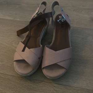 Klackar  med kilklack - Snygga rosa sandaler med kilklack och korsade remmar. De har ett spänne vid ankeln för justerbar passform. Perfekta för sommarens alla tillfällen. Endast använda på ett bröllop så därför i nyskick 