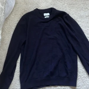 Mörkblå tröja från These Glory Days - Snygg och stilren mörkblå tröja från These Glory Days i Superior Merino. Perfekt för kyligare dagar med sin mjuka och bekväma passform. Tröjan har långa ärmar och en klassisk rund halsringning.