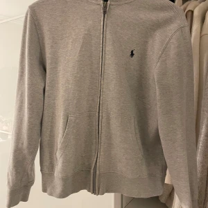 Grå hoodie från Ralph Lauren - Säljer en zip hoodie från Ralph Lauren. Den är i 14-16 år men motsvarar typ xs. Den är i fint skick.