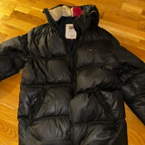 Svart pufferjacka Tommy Hilfiger - En svart Tommy Hilfiger pufferjacka som är i mycket bra skick, den är lite smutsig på den vita delen av kragen men det går att rengöra. 