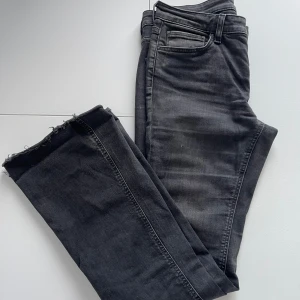 Grå/Svarta bootcut jeans lågmidjat  - Lågmidjade Grå/ svarta bootcut jeans med rå kant och klassisk femficksdesign. Avklippta och slitna nertill men passar designen. Perfekta för en avslappnad stil med en touch av edge. Passar bra till både sneakers och klackar. Strl 40 passar mer en 38. Midja 39cm. Innerben 78/79 cm. 