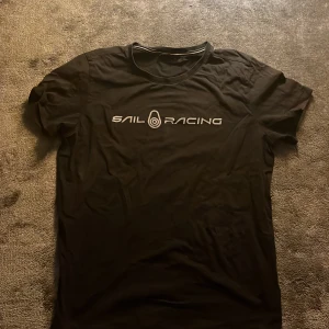 Svart t-shirt från Sail Racing - Snygg svart t-shirt från Sail Racing med deras logga tryckt på bröstet. Perfekt för en avslappnad stil. Kortärmad och i en klassisk passform.