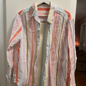 Randig skjorta från Bik Bok - Säljer en färgglad randig skjorta från Bik Bok i storlek S. Skjortan har långa ärmar och en klassisk krage. Färgerna inkluderar rosa, blå, gul och orange, vilket ger en somrig känsla. 