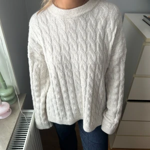 Vit stickad tröja - Mysig vit stickad tröja med kabelstickat mönster. Perfekt för kyliga dagar med sin klassiska design och bekväma passform. Långärmad och rund halsringning.
