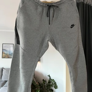 Nike Tech Fleece -   Nike Tech Fleece byxor  med svart logga på benet. Byxorna har en bekväm passform med dragsko i midjan för justerbarhet. Perfekta för en avslappnad stil.