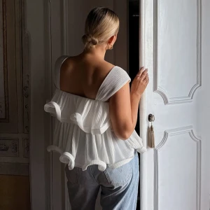 Volang topp!! Lojsan Wallin x NA-KD - Säljer den stilrena populära vita toppen från NA-KD med volangdetaljer i Lojsan Wallins kollektion. Toppen har breda axelband, luftig passform och ett innertyg.☀️ Helt slutsåld på hemsidan. Använd en gång. 🤍💛