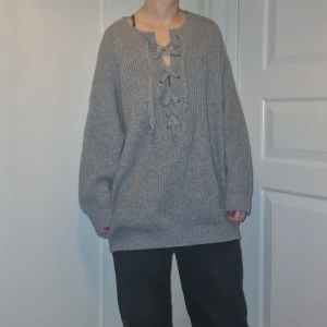Grå stickad tröja med snörning - Mysig grå stickad tröja med snörning framtill. Tröjan har en oversized passform och långa ärmar, perfekt för kyliga dagar. Endast användas en gång av mig, passar xs-xl beroende på vad för passform du vill ha. Personen på bilden har storlek s. Pris går att diskutera.