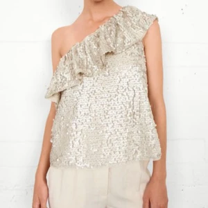 Glittrig oneshoulder topp second Female  - Snygg glittrig oneshoulder topp med volangdetalj. Perfekt för en festlig kväll. Den har en lös passform och är täckt med paljetter som ger en lyxig känsla. Storlek m men ser ut som s