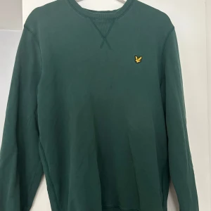 Grön sweatshirt från Lyle & Scott - Säljer en snygg grön sweatshirt från Lyle & Scott med deras ikoniska logga på bröstet. Tröjan har långa ärmar och en ribbad krage. Perfekt för en avslappnad stil.