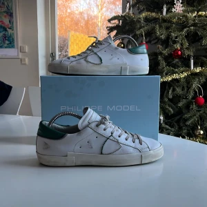 Vita sneakers från Philippe Model - Snygga vita sneakers från Philippe Model med gröna detaljer och snörning. Skorna har en klassisk design med en modern twist och kommer med originalförpackning och dustbag. Köpta för 3500 kr på cettire riktigt bra skick hälen är lite sliten men de är inget man tänker på. Hör av er vid minsta lilla fråga mvh Hugo😄