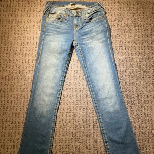 Blå jeans från True Religion - Snygga blå jeans från True Religion med ikonisk broderad design på bakfickorna. De är bootcut. Midja rakt över: 36cm. Lår: 25cm. Innerben: 83cm