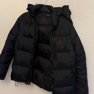 Svart dunjacka från Polo Ralph Lauren - Säljer en svart dunjacka från Polo Ralph Lauren. Jackan har en pufferdesign med dragkedja och huva, perfekt för kyliga dagar. Jag säljer jackan eftersom den har börjat bli för liten för mig, där jag har haft den sedan somras. Jag köpte den i somras inför vintern så har inte använt den alls men har märkt att den är för liten. Orginal priset var 4990kr. Storleken är M. priset kan diskuteras men går inte lägre än 2000kr. 