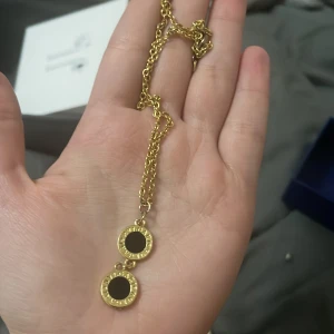 Guldhalsband med svarta detaljer - Elegant guldhalsband med två runda hängen i svart och guld. Perfekt för att ge en stilren touch till din outfit.