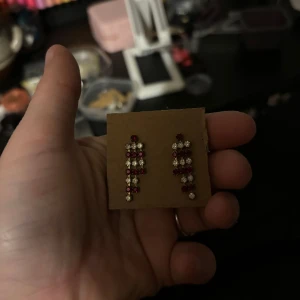 Glittriga örhängen med röda och vita stenar - Snygga glittriga örhängen med en kombination av röda och vita stenar. Perfekta för att ge en extra touch till din outfit. De har en hängande design som ger en elegant look.