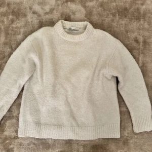 Vit stickad tröja från Zara - Mysig vit stickad tröja från Zara med rund hals och långa ärmar. Perfekt för kyliga dagar och enkel att matcha med jeans eller kjol. Lite lite nopprig!