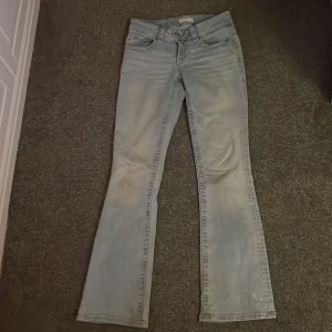 Ljusblå bootcut jeans - Snygga ljusblå bootcut jeans med klassisk femficksdesign och knappdetaljer på bakfickorna. Perfekta för en avslappnad stil. Lite slitningar längst ner men inget man tänker på när dom används.