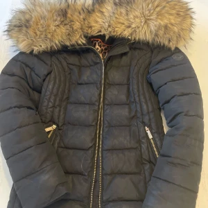 Svart dunjacka med päls från Roco Baroco - Snygg svart dunjacka från Roco Baroco med en mysig pälsfodrad huva. 