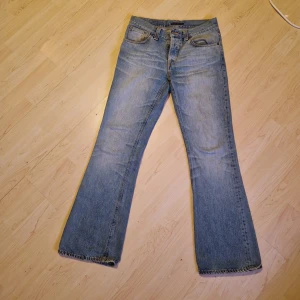 Blå jeans från Nudie - Säljer ett par klassiska blå jeans från Nudie utsvängda, bootcut. De har en knappgylf och snygga detaljer på bakfickorna. 