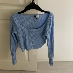 Ljusblå ribbad tröja från Divided - Säljer en ljusblå ribbad tröja från Divided. Tröjan har en croppad design med långa ärmar och en rundad halsringning. Perfekt för en stilren och bekväm look.