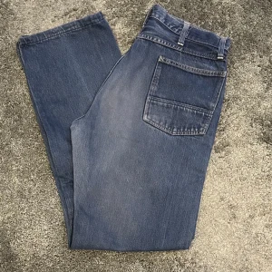 Vintage jeans från Replay 29”34 - Säljer ett par klassiska blå jeans från Replay. De har en straight passform och är tillverkade i denim. Byxorna har en knappgylf och femficksdesign, vilket ger dem en tidlös look. Storlek 29 i midjan, 34 i längd.