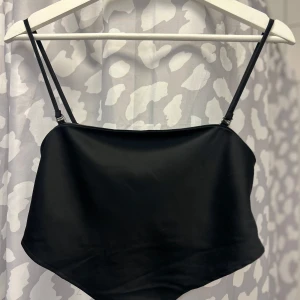 Svart axelbandslös tubtopp - Snygg svart tubtopp med smala axelband och elastisk smockdetalj på baksidan. Perfekt för en stilren look.
